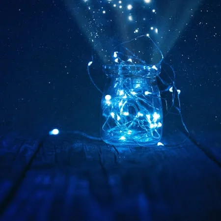 Glas mit blauen Lichtern auf einer Holzoberfläche vor dunklem Hintergrund