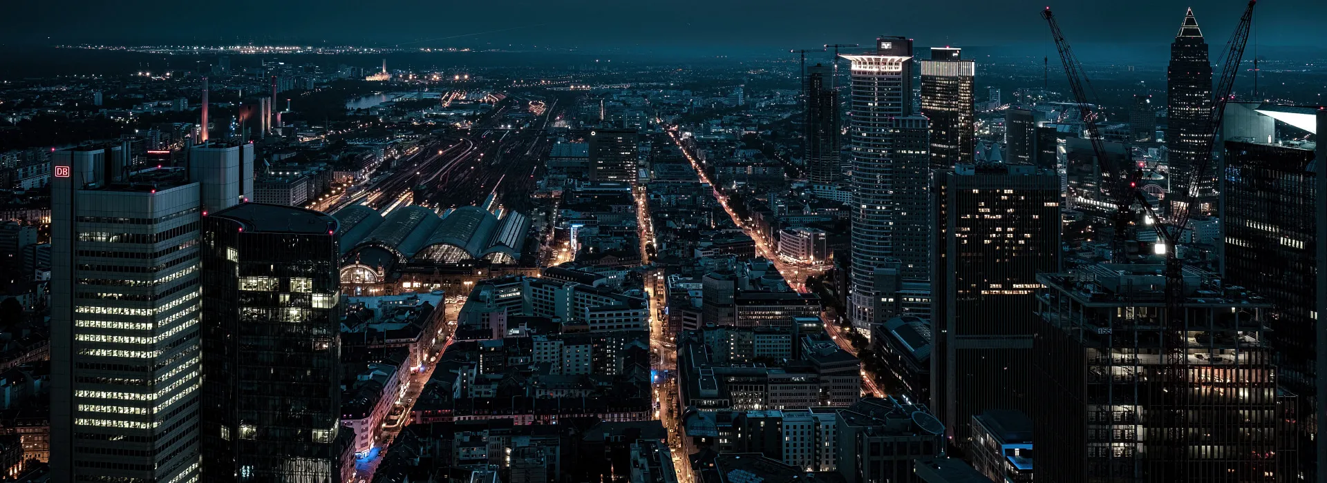 Blick auf eine nächtliche Stadtlandschaft mit beleuchteten Straßen und Hochhäusern.